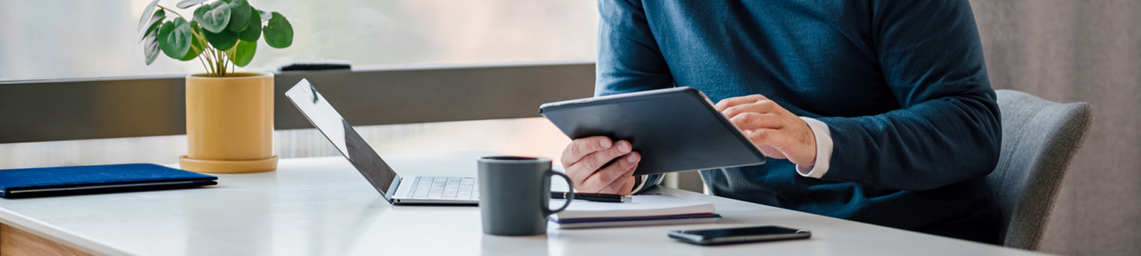 Cropped image of man using tablet at desk with laptop and phone